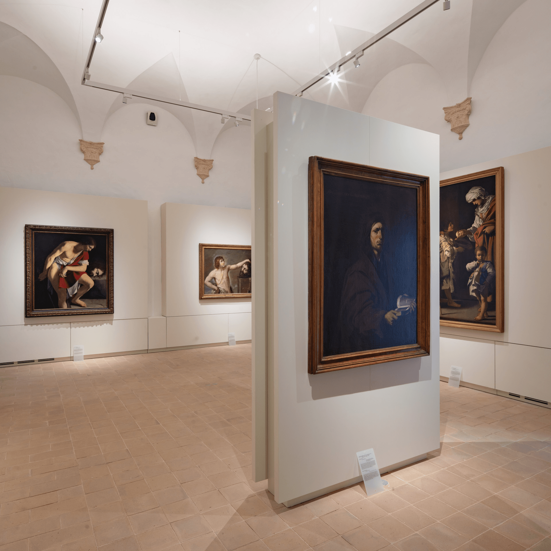 Ampia sala museale con soffitti a volta e grandi dipinti barocchi esposti su pannelli centrali e lungo le pareti illuminate da faretti.