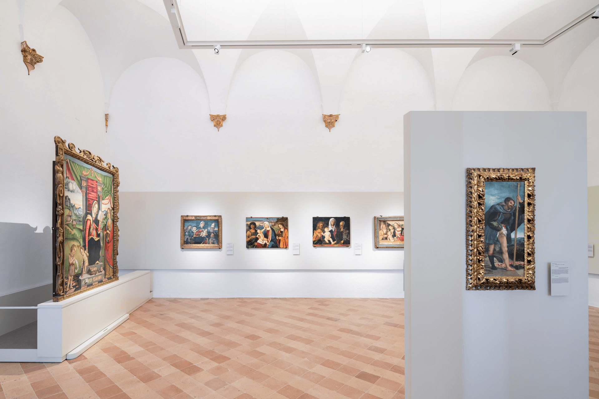 Sala del museo con pavimento in cotto e pareti bianche, allestita con dipinti rinascimentali e una grande pala d’altare decorata esposta lateralmente.
